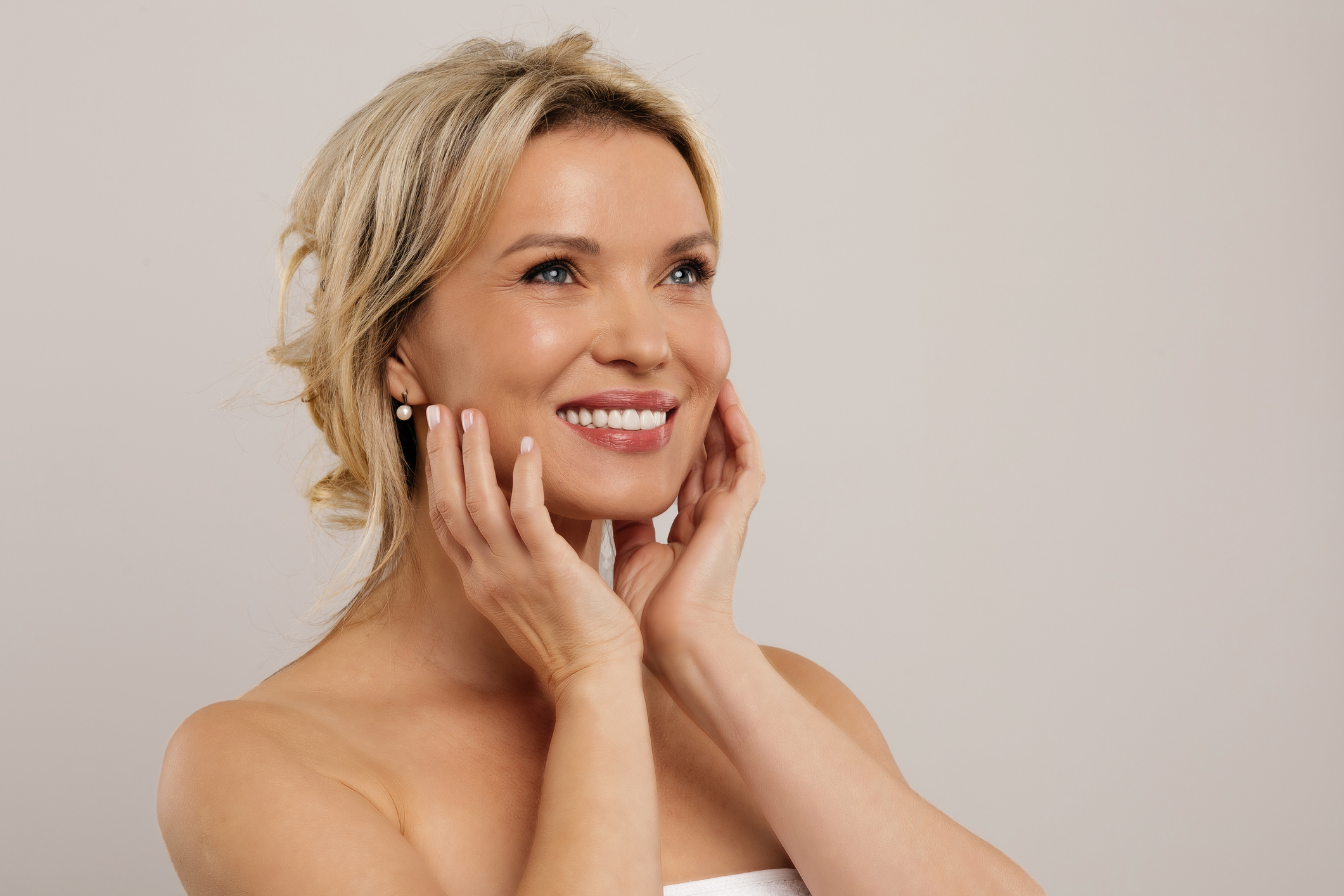 Closeup of middle aged blonde woman isolated on grey background, smiling beautiful